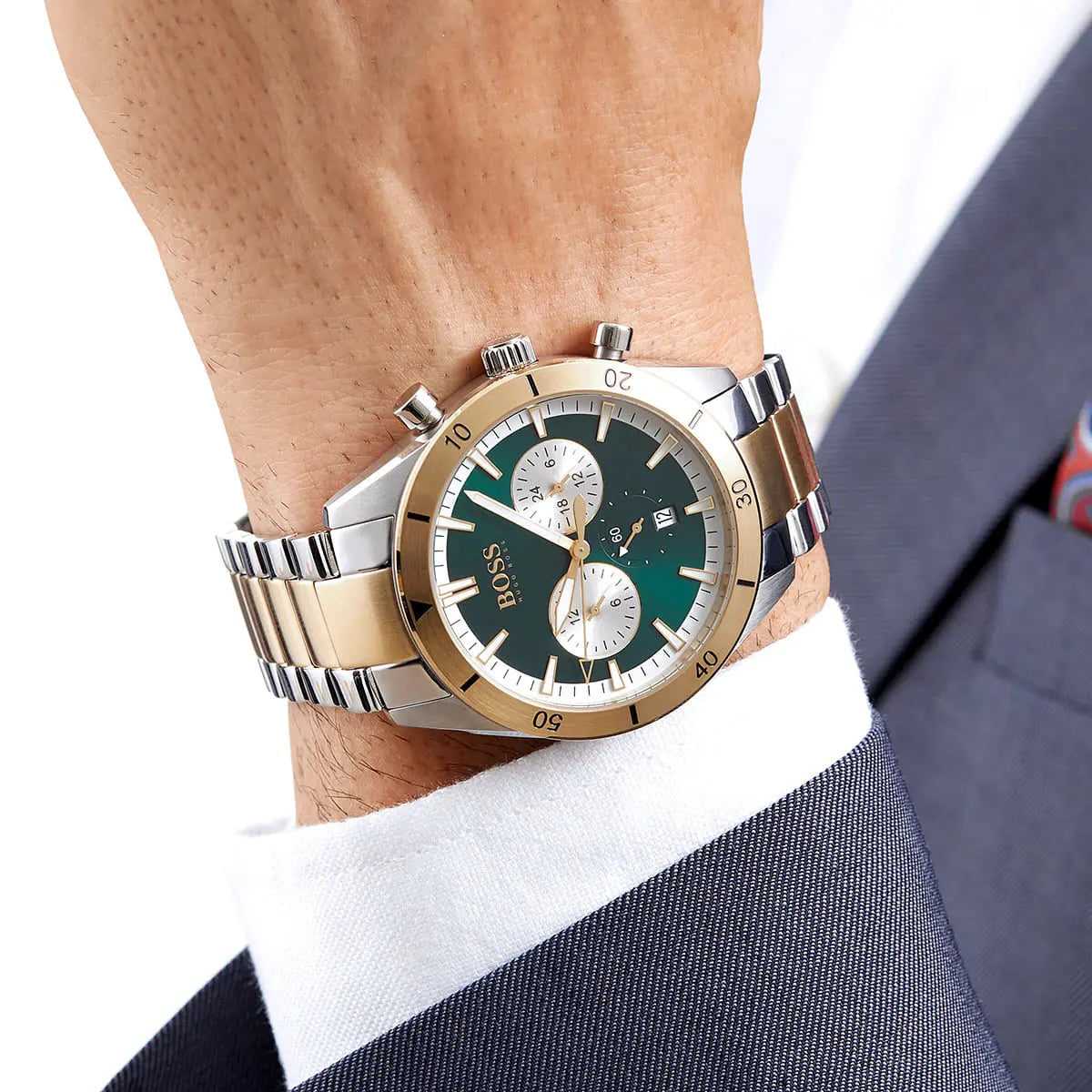 Luxury watch with green face and gold accents on a person's wrist, wearing a suit.